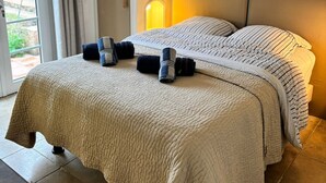 Ein Doppelbett mit gestepptem Kopfteil, ein Nachttisch und ein Blick ins Freie durch eine Schiebetür.