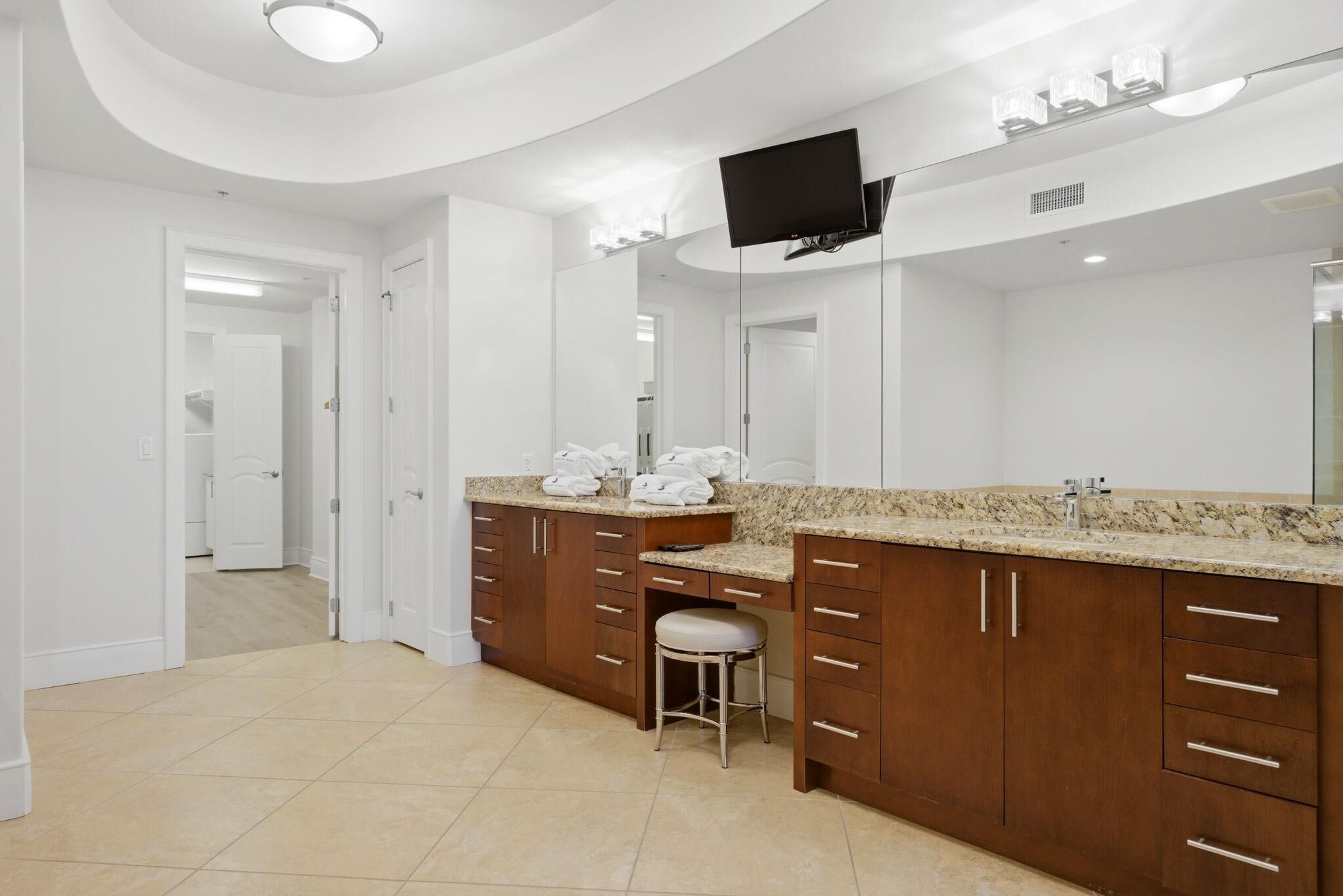 A bathroom with a large mirror, a vanity with a sink, and a stool.