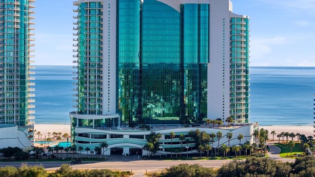 A modern hotel with a curved glass facade, multiple balconies, and a beachfront location. - Turquoise C2509 (Orange Beach)