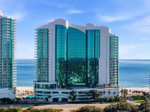 Un hôtel moderne doté d’une façade en verre incurvée, de nombreux balcons et situé en bord de mer.