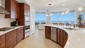A modern kitchen with a large island, built-in oven, and a view of the ocean. - Turquoise C2509 (Orange Beach)
