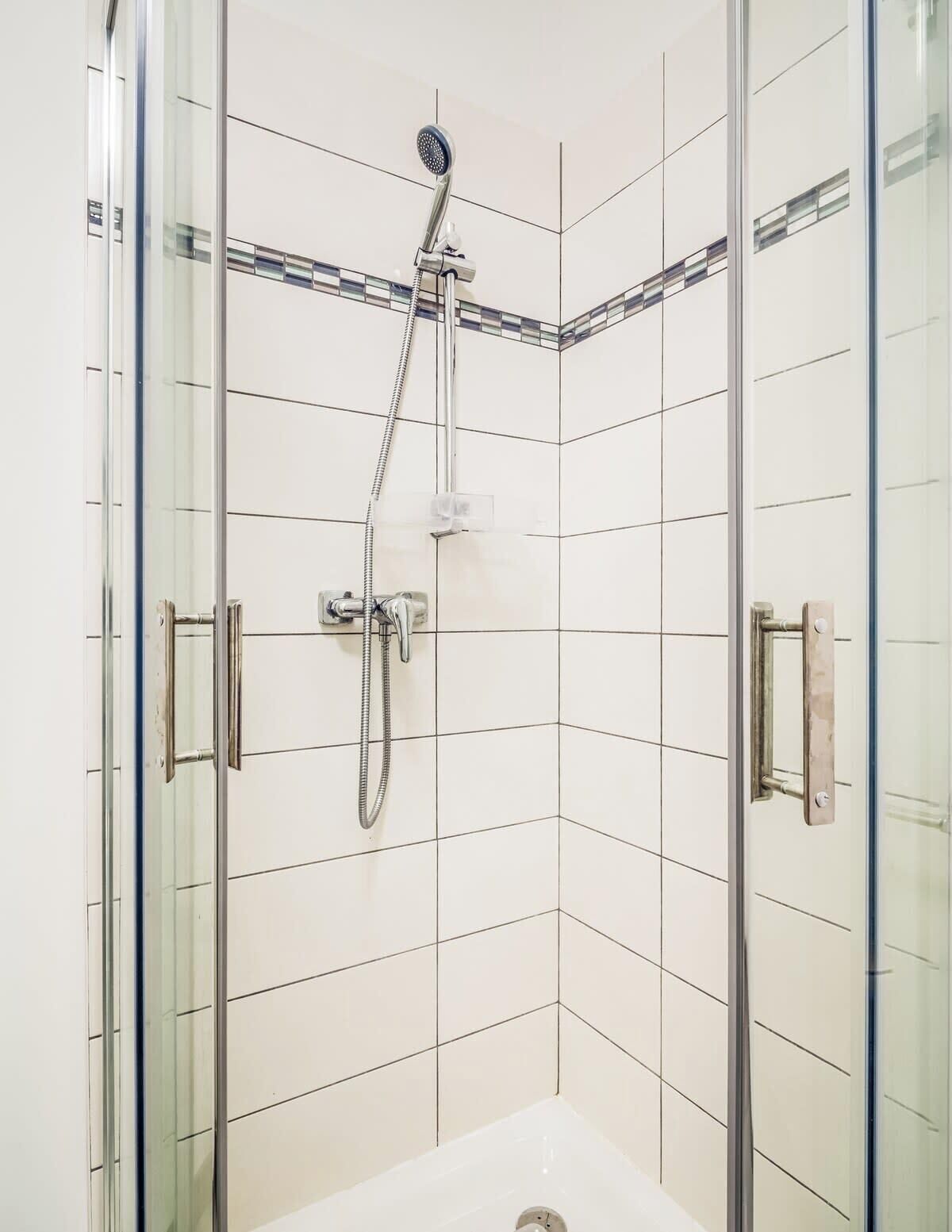 A glass-enclosed shower with a handheld showerhead and a wall-mounted faucet.