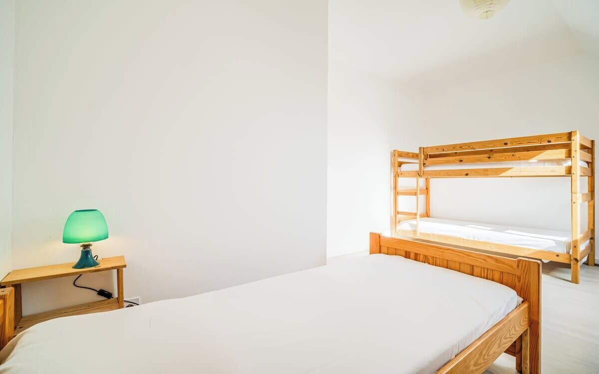 A simple room with a bunk bed, a bedside table with a lamp, and a plain white wall.