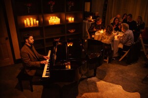 Un pianista en una habitación con poca luz, con un grupo de personas sentadas a una mesa.