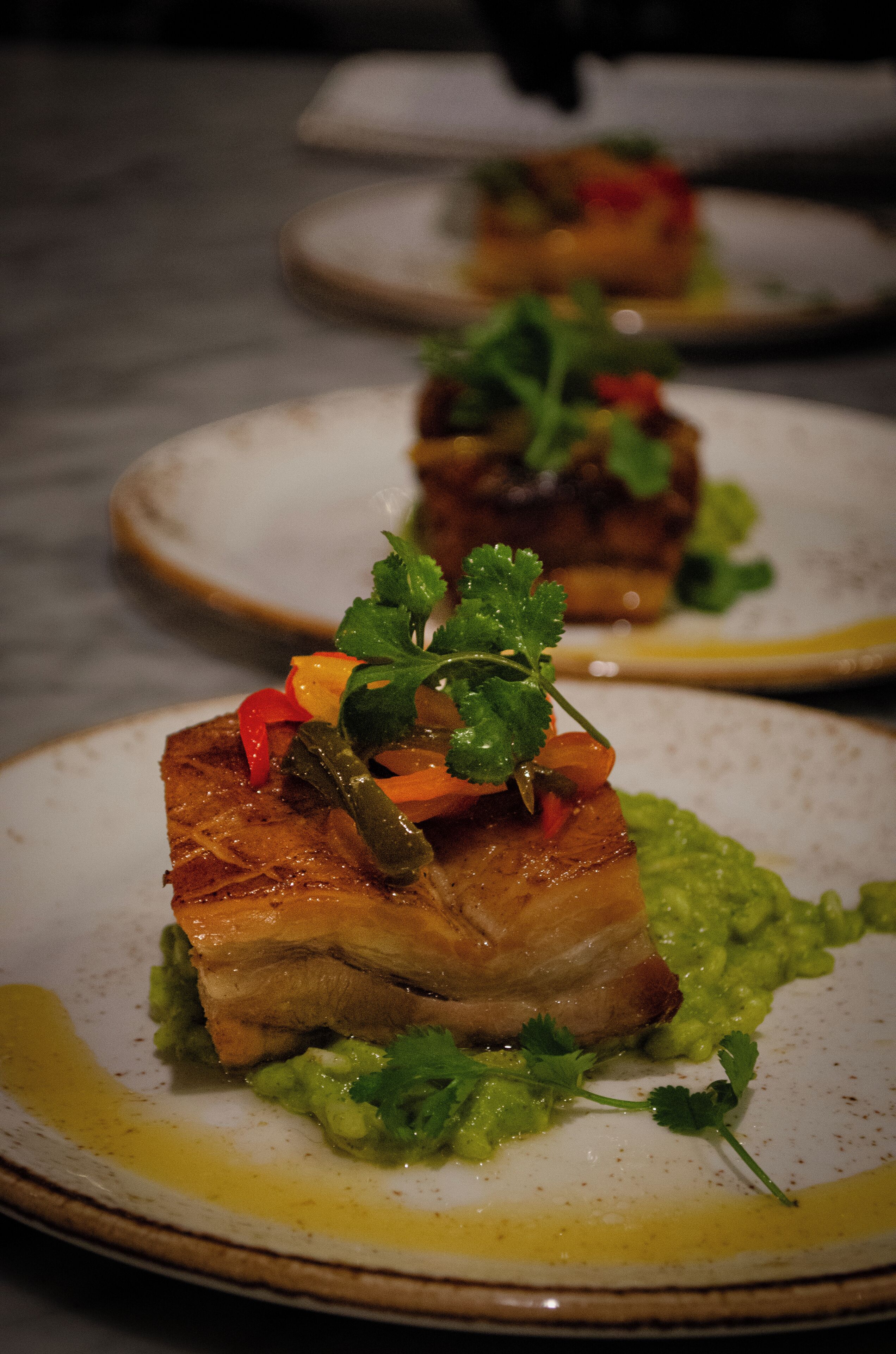 Une assiette contenant un morceau de viande, recouvert de légumes et agrémenté d’herbes.