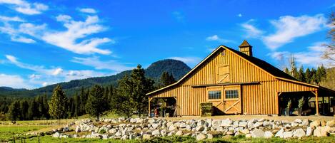 A wooden barn with a large open garage, surrounded by a stone wall and a grassy field.