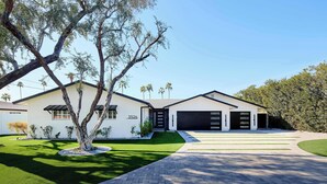 A modern two-story house with a well-maintained lawn, a driveway leading to a garage, and palm trees in the background. - Velvet Spur | Designer Stay in Old Town! Walkable (Scottsdale)