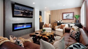 A modern living room with a flat-screen TV, a fireplace, leather sofas, and a wooden accent wall. - Velvet Spur | Designer Stay in Old Town! Walkable (Scottsdale)