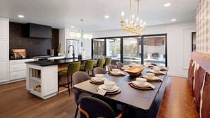 A modern kitchen with a central island, bar seating, and a dining area with a long table set for six. - Velvet Spur | Designer Stay in Old Town! Walkable (Scottsdale)