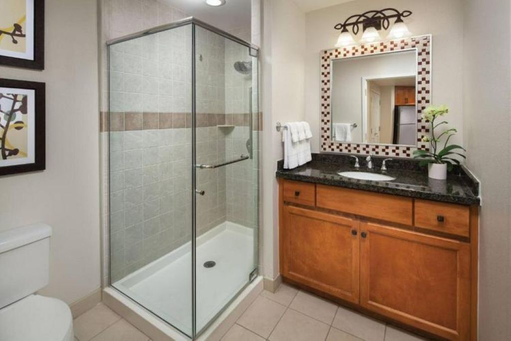Un baño con ducha de vidrio, tocador de madera con lavamanos y espejo con marco decorativo.