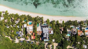 Vista aérea de un complejo turístico costero con varias construcciones, una playa de arena y un mar turquesa cristalino.