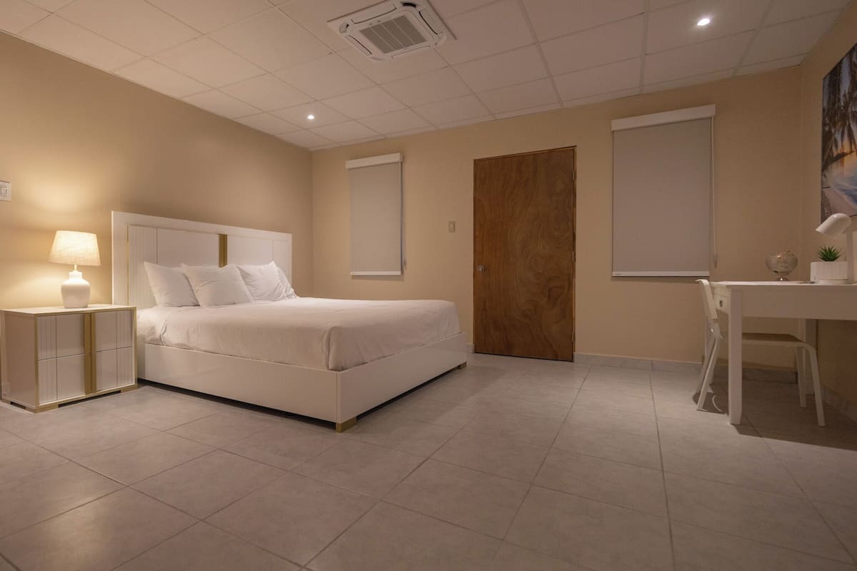 A hotel room with a bed, bedside table, desk, chair, and a door.