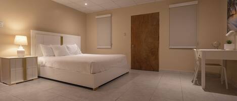 A hotel room with a bed, bedside table, desk, chair, and a door.