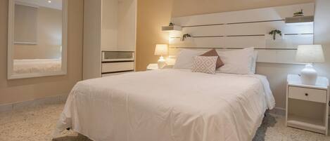 A bedroom with a large bed, bedside tables, a mirror, and a wall-mounted shelf with plants.