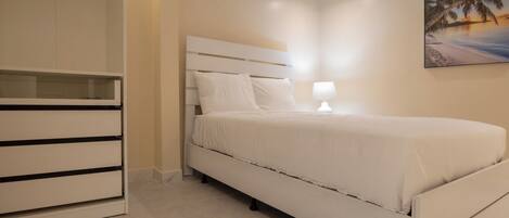 A bedroom with a bed, a nightstand, a lamp, and a painting of a beach scene.