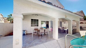 Un patio techado al aire libre con piscina, que cuenta con un comedor con sillas y una mesa, y una zona de estar con sofás y televisor.