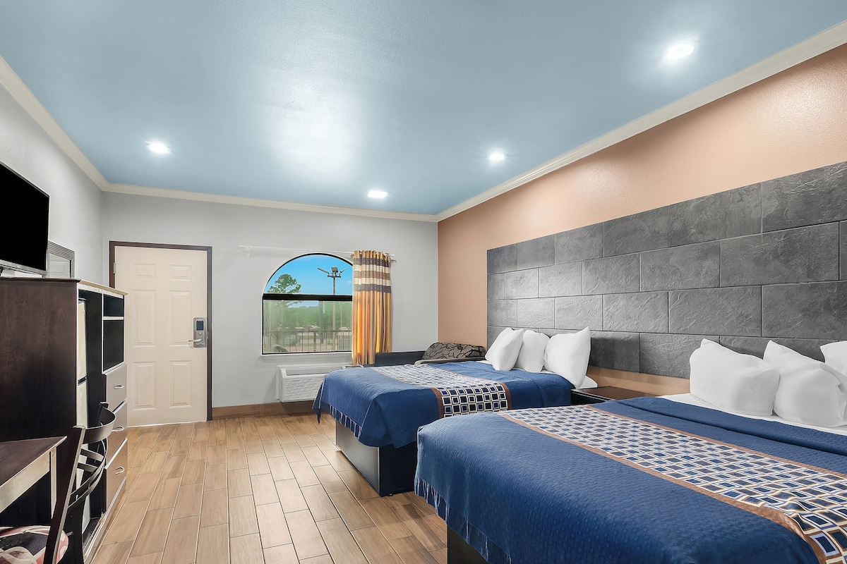A hotel room with two beds, a TV, a window with curtains, and a view of the outdoors.