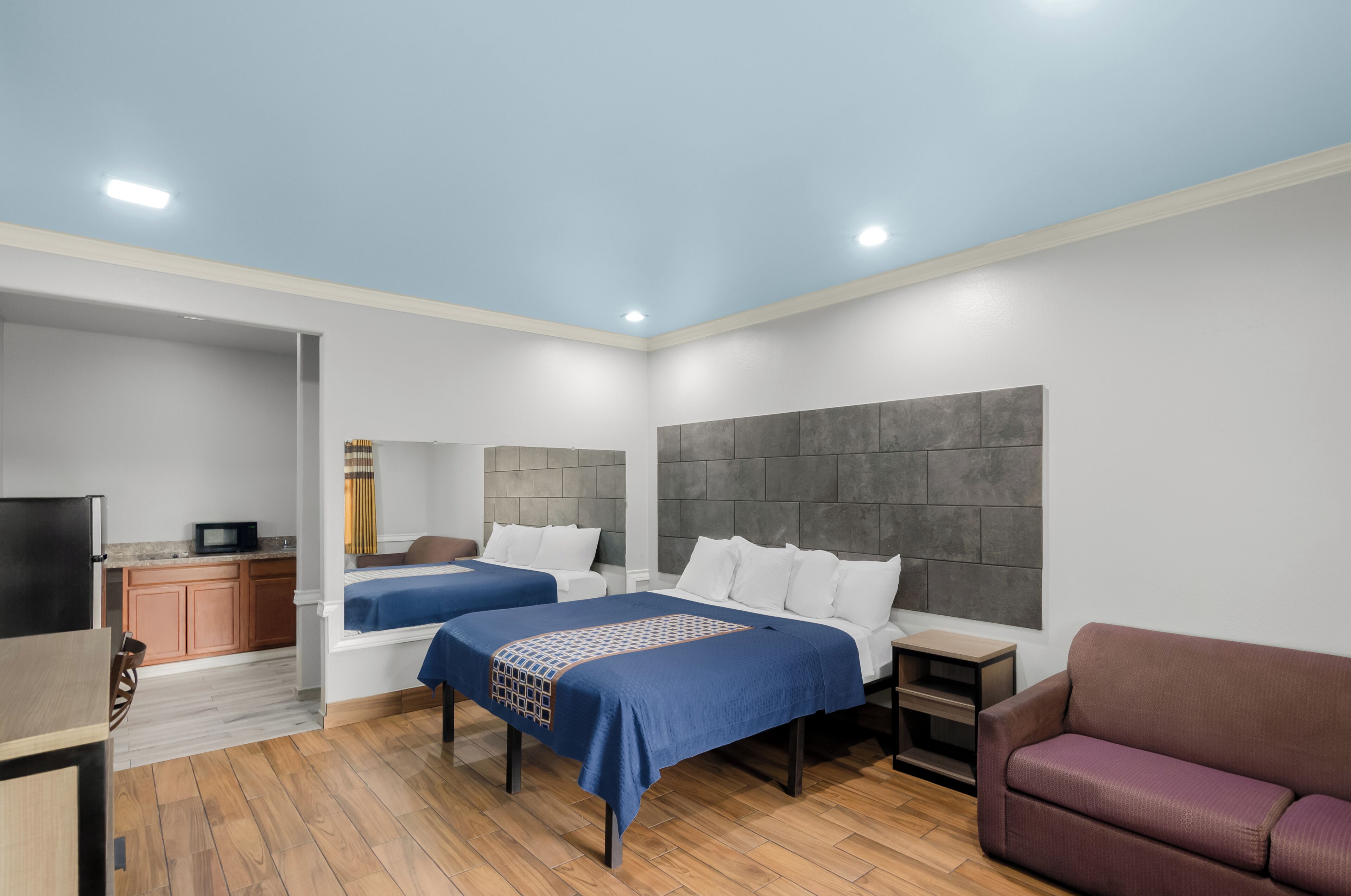 A modern hotel room with two beds, a TV, a small kitchenette, and a seating area.