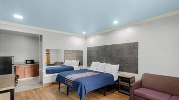 A modern hotel room with two beds, a TV, a small kitchenette, and a seating area.