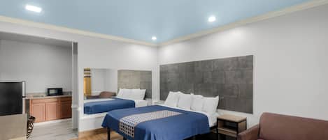 A modern hotel room with two beds, a TV, a small kitchenette, and a seating area.