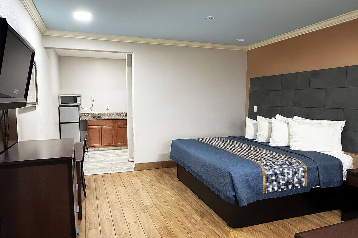 A hotel room with a bed, a desk, a TV, a kitchenette, and a bathroom.