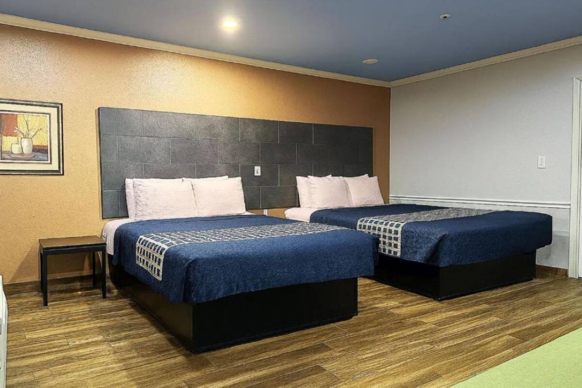 A hotel room with two beds, a headboard, a small table, and a painting on the wall.