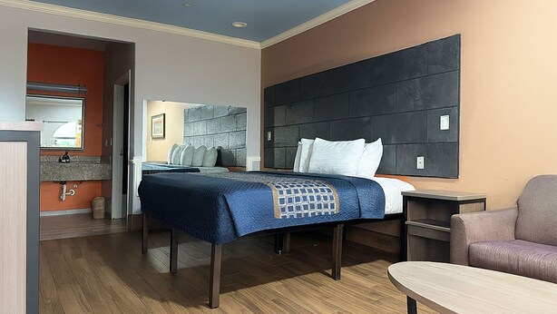 Une chambre d’hôtel avec un lit, un bureau, une chaise et une salle de bain visible à travers une porte ouverte.