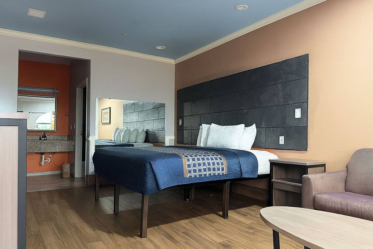A hotel room with a bed, a desk, a chair, and a bathroom visible through an open door.