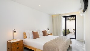 A bedroom with a bed, bedside tables, a nightstand, a patterned rug, and a view of the outdoors through a door. - Beachside Bliss: Carcavelos 1Br W/Patio & Parking (Cascais)