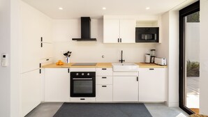 A modern kitchen with white cabinets, a black oven, a microwave, and a sink. - Beachside Bliss: Carcavelos 1Br W/Patio & Parking (Cascais)