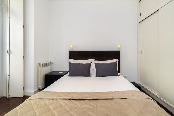 Ein Schlafzimmer mit Bett, Nachttischen, einem Heizkörper und einer Tür.