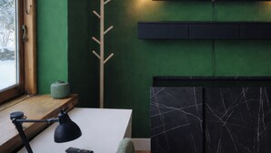 Ein Zimmer mit grüner Wand, einem an der Wand montierten Fernseher, einem Holztisch mit Lampe und einer schwarzen Schrankumrandung.