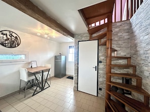 Une cuisine avec une table à manger, un réfrigérateur, un escalier en bois et un mur en pierre.