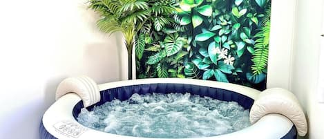 A hot tub with a blue interior and white exterior, surrounded by a wall with a tropical plant mural.