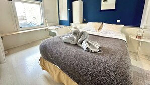 Un dormitorio con una cama grande, una ventana, una mesita de noche y un velador.