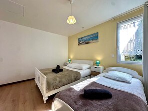 Une chambre avec deux lits, un tableau, une fenêtre avec des rideaux en dentelle et un luminaire suspendu.