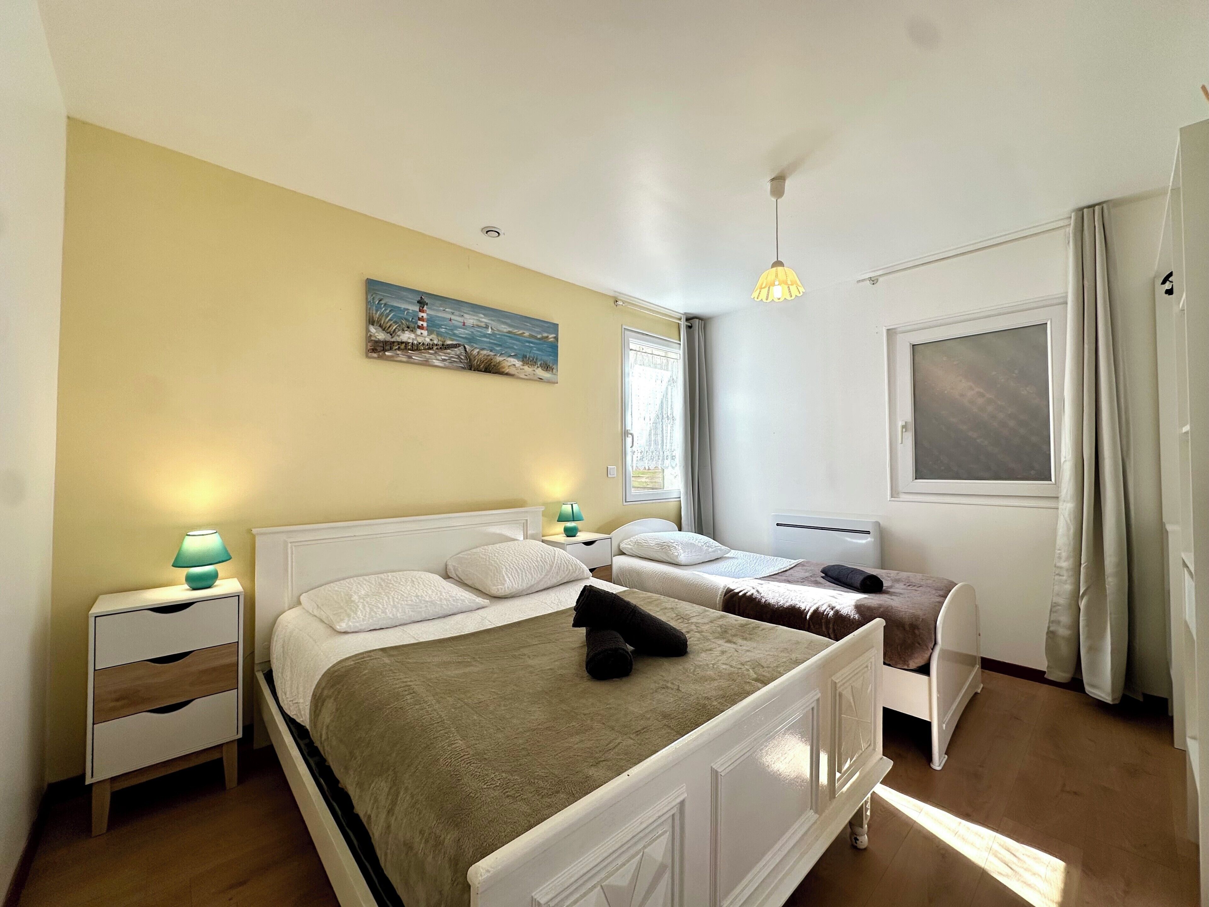 Une chambre avec deux lits, un tableau, une fenêtre avec des rideaux et un luminaire au plafond.