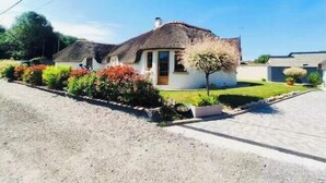 Une maison à toit de chaume, avec un petit jardin devant et une allée pavée.