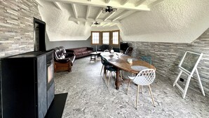 Un loft spacieux avec de hauts plafonds, des poutres apparentes, une cheminée, un coin repas avec une table et des chaises en bois, et un coin salon avec un canapé en cuir.
