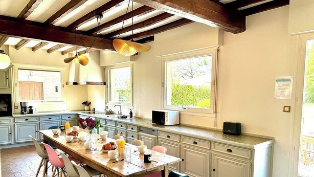 A spacious kitchen with a large island, white cabinetry, and a dining area with colorful chairs.
