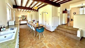 A spacious kitchen with a dining area, featuring a stone floor, wooden beams, and modern appliances.
