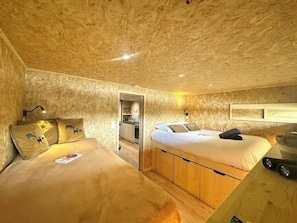 A cozy room with a bed, a wooden desk, and a small kitchenette.