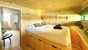 Un dormitorio con una cama nido de madera, una mesita pequeña y un espejo con marco verde.
