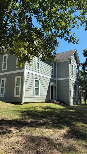 A two-story house with a grey siding exterior, a front porch, and a visible number '74' on the front door. - Emerald Hour Loft: 2 mins from UNA (Florence)