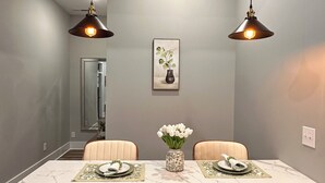 A modern kitchen with dark cabinets, a marble countertop, and pendant lighting.