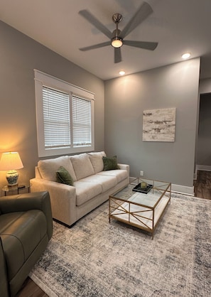 A living room with a beige sofa, a coffee table, a lamp, and a ceiling fan.