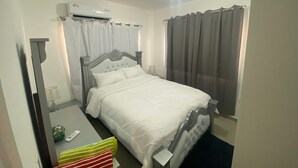 A hotel room with a bed, a bedside table, a mirror, and a window with curtains. - Lovely 2-bedroom apartment with AC in charming Bayahíbe 125 DOLARES POR NOCHE (Bayahíbe)