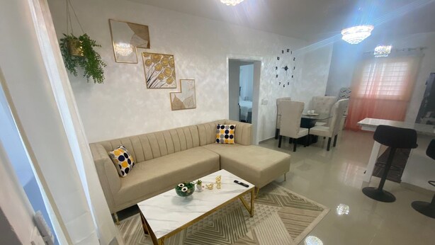 A modern living room with a beige sofa, a coffee table, and a dining area with chairs and a table. - Lovely 2-bedroom apartment with AC in charming Bayahíbe 125 DOLARES POR NOCHE (Bayahíbe)