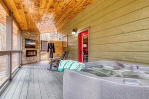 Eine Holzterrasse mit Kamin aus Stein, einem Whirlpool und einer roten Tür.