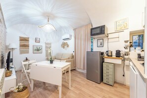 A compact kitchen with a refrigerator, microwave, and a small countertop. There is a dining area with a white table and chairs. - BHM Urban House Pigneto (Rome)